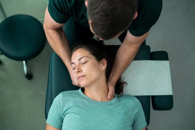 Vista de cima de um quiroprata manipulando a coluna cervical de um paciente deitado.