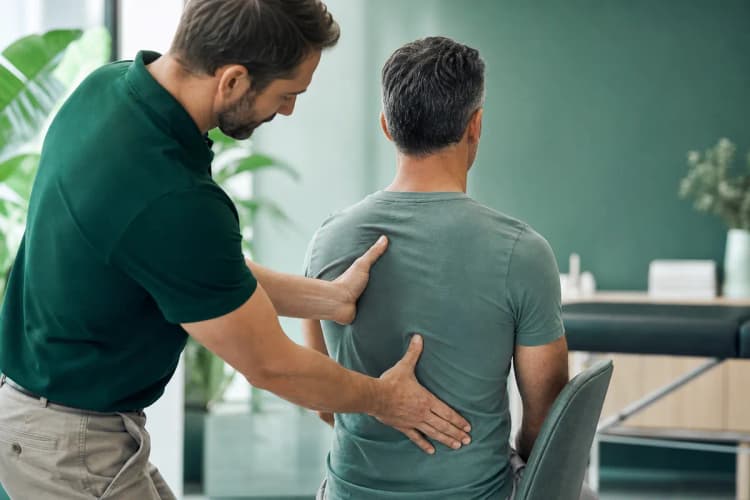Um quiroprata examinando a coluna de um paciente com as mãos, em um consultório médico.