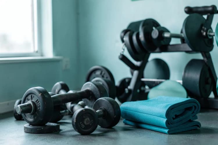 Um conjunto de pesos de academia e um tapete de yoga dobrado em um canto.